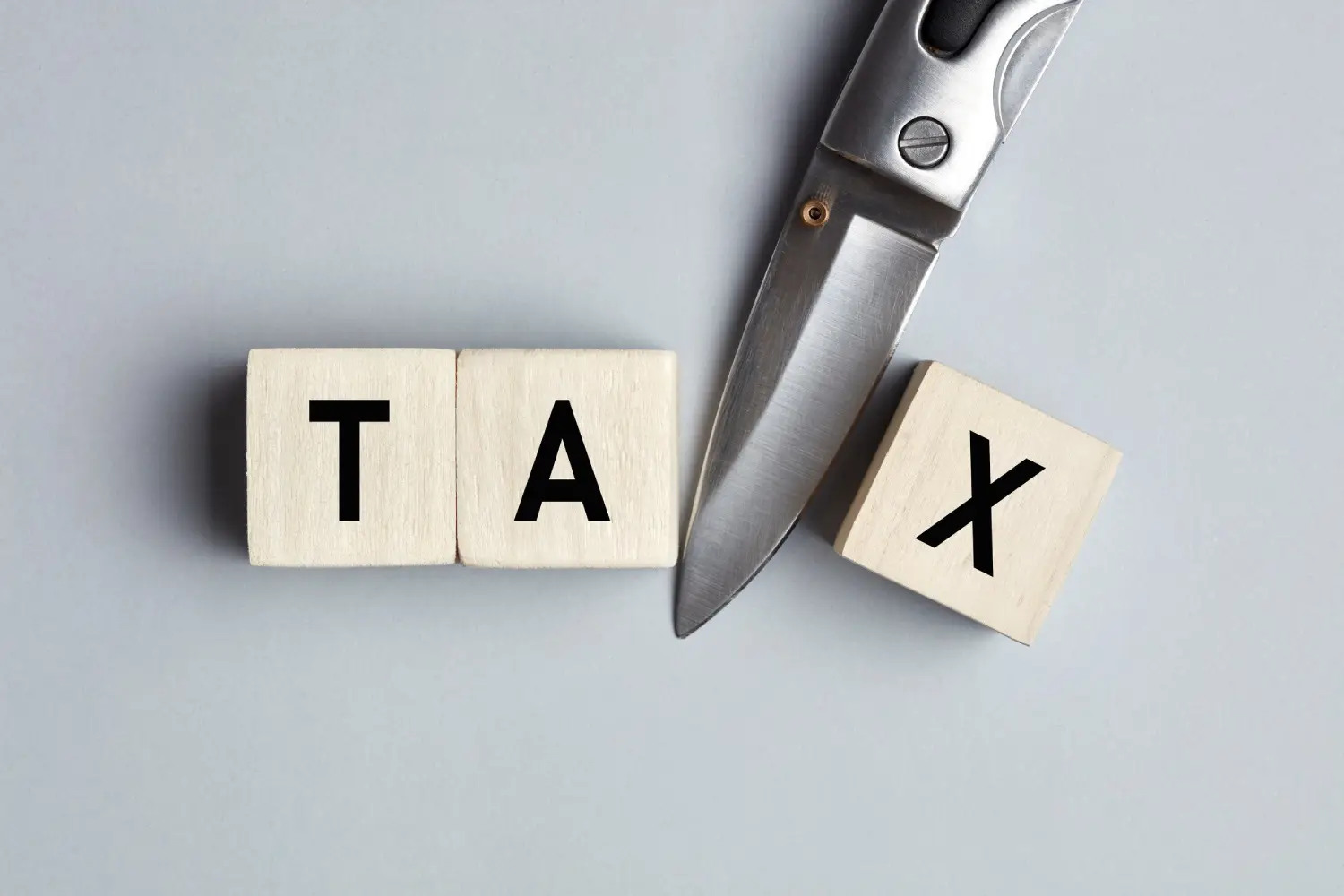 Wooden blocks spelling TAX beside a knife, representing cutting your tax bill